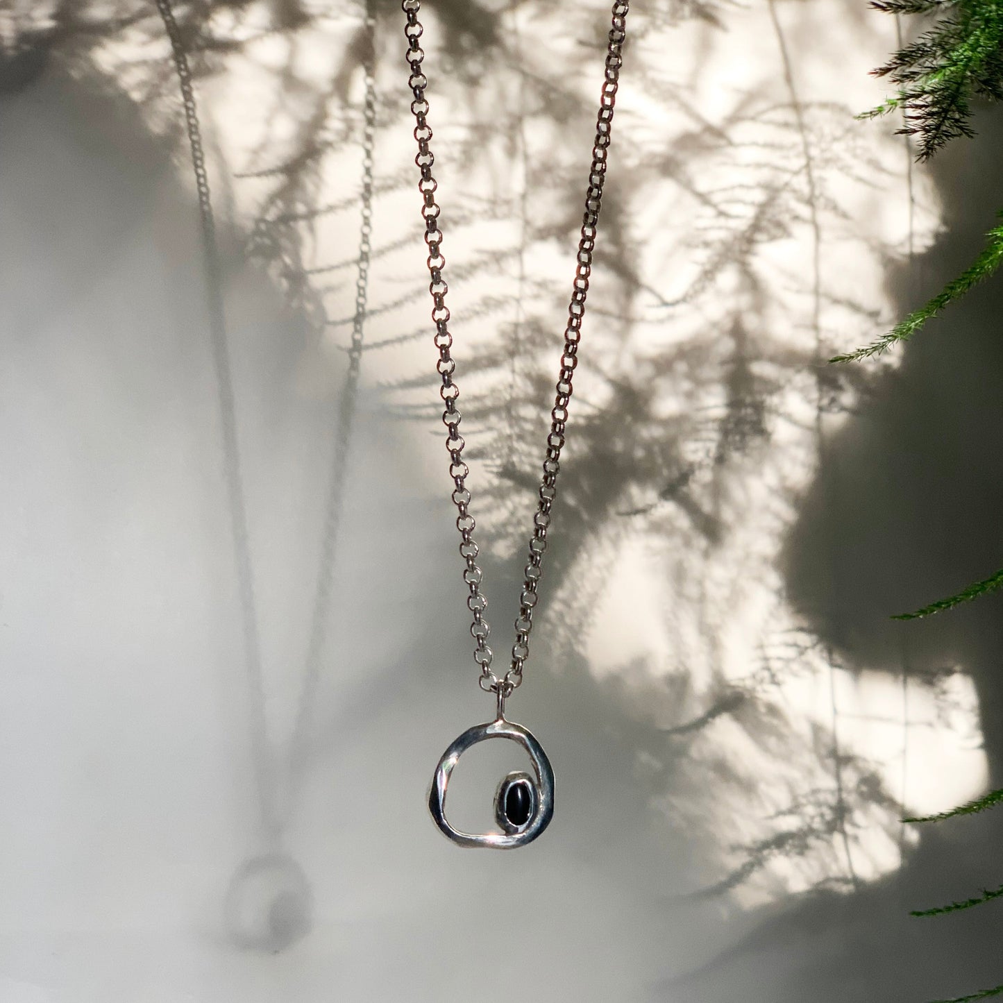sterling silver pendant necklace with circular organic form pendant featuring an onyx gemstone set to bottom inner right hand corner